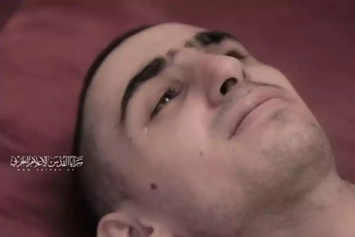Man lying on a red surface with a tear on his cheek and a serious expression