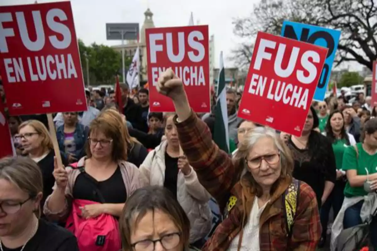 Manifestación de personas con carteles rojos que dicen FUS en lucha y una mujer mayor levantando el puño en señal de protesta Manifestación de personas con carteles rojos que dicen FUS en lucha y una mujer mayor levantando el puño en señal de protesta