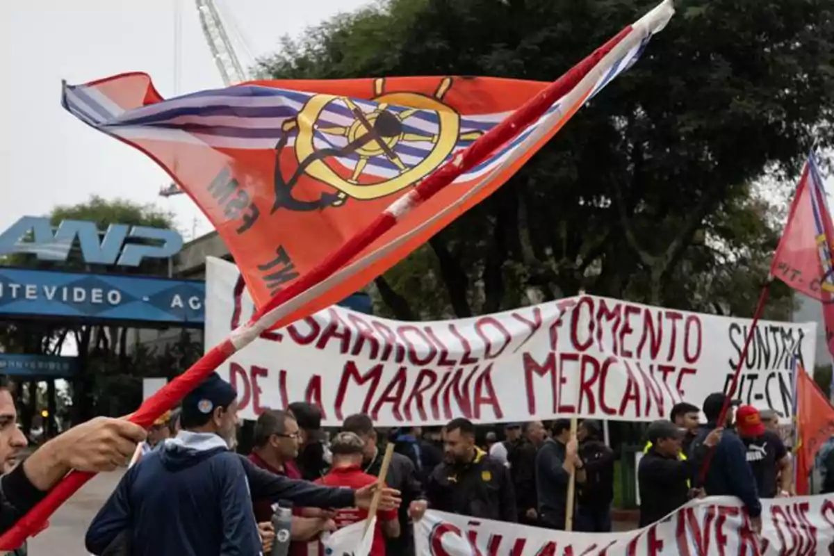 Personas manifestándose frente a la entrada de la Administración Nacional de Puertos con banderas y pancartas que piden desarrollo y fomento de la marina mercante