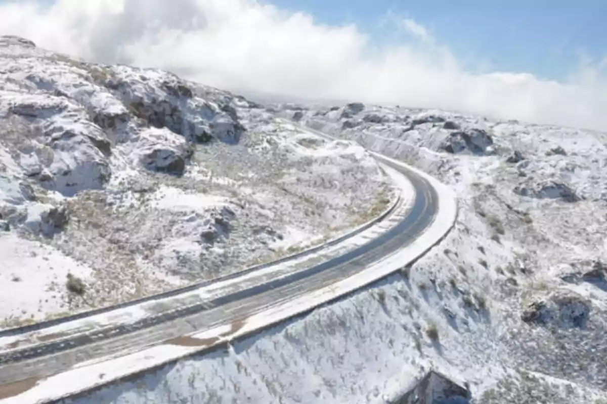 Carretera sinuosa en una zona montañosa cubierta de nieve bajo un cielo parcialmente nublado Carretera sinuosa en una zona montañosa cubierta de nieve bajo un cielo parcialmente nublado