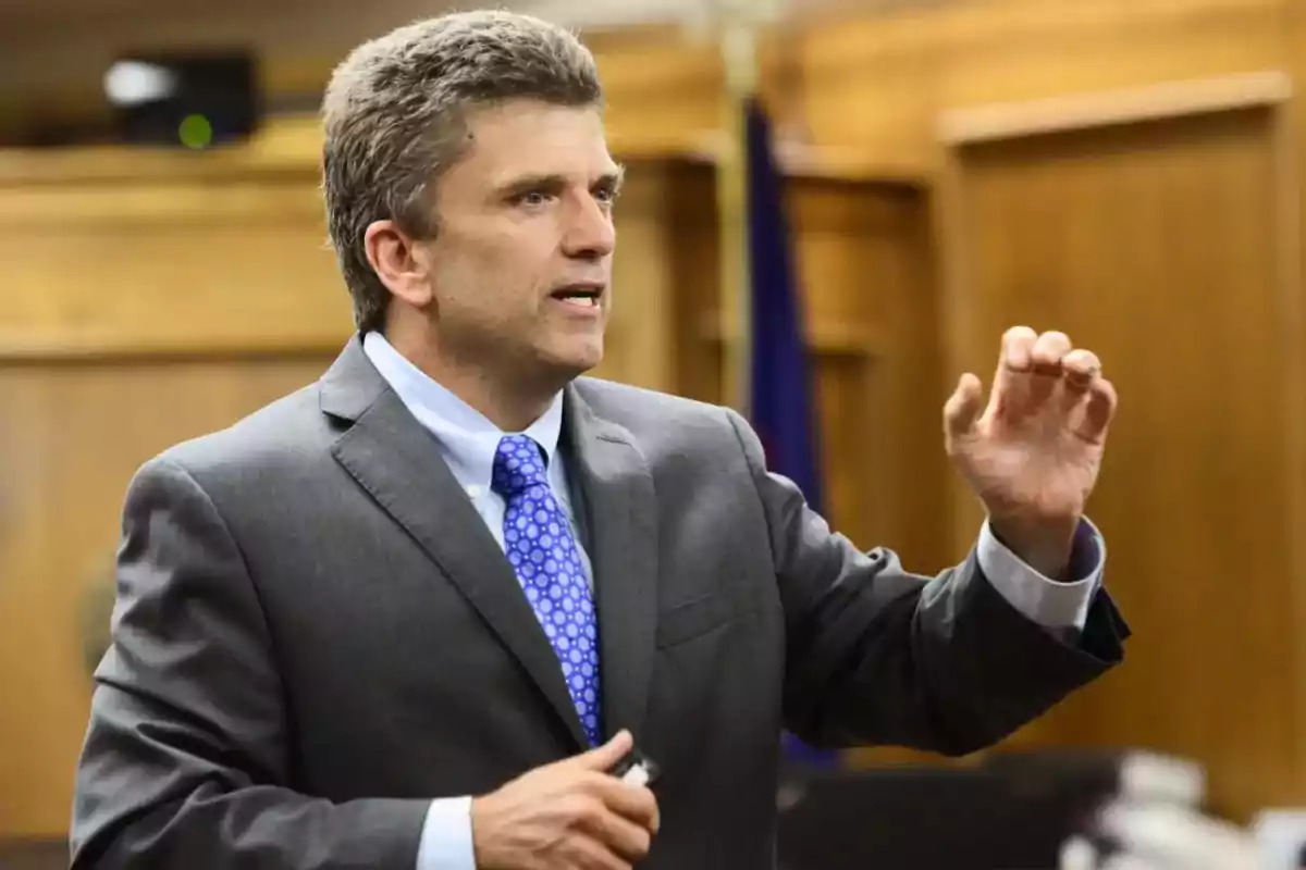 Hombre de traje gris y corbata azul hablando y gesticulando en una sala de tribunal Hombre de traje gris y corbata azul hablando y gesticulando en una sala de tribunal