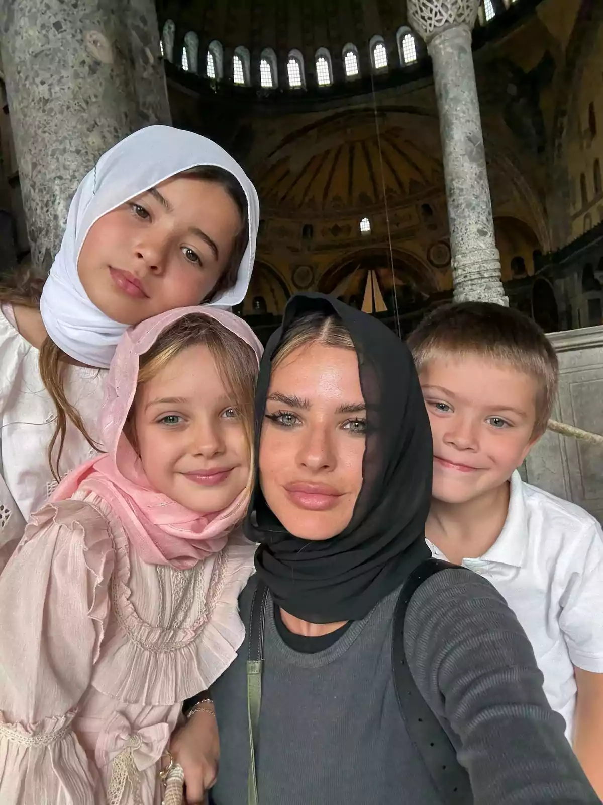 Cuatro personas, tres niñas y un niño, posan para una selfie dentro de un edificio histórico con columnas y cúpula, algunas de ellas llevan velo en la cabeza. Cuatro personas, tres niñas y un niño, posan para una selfie dentro de un edificio histórico con columnas y cúpula, algunas de ellas llevan velo en la cabeza.