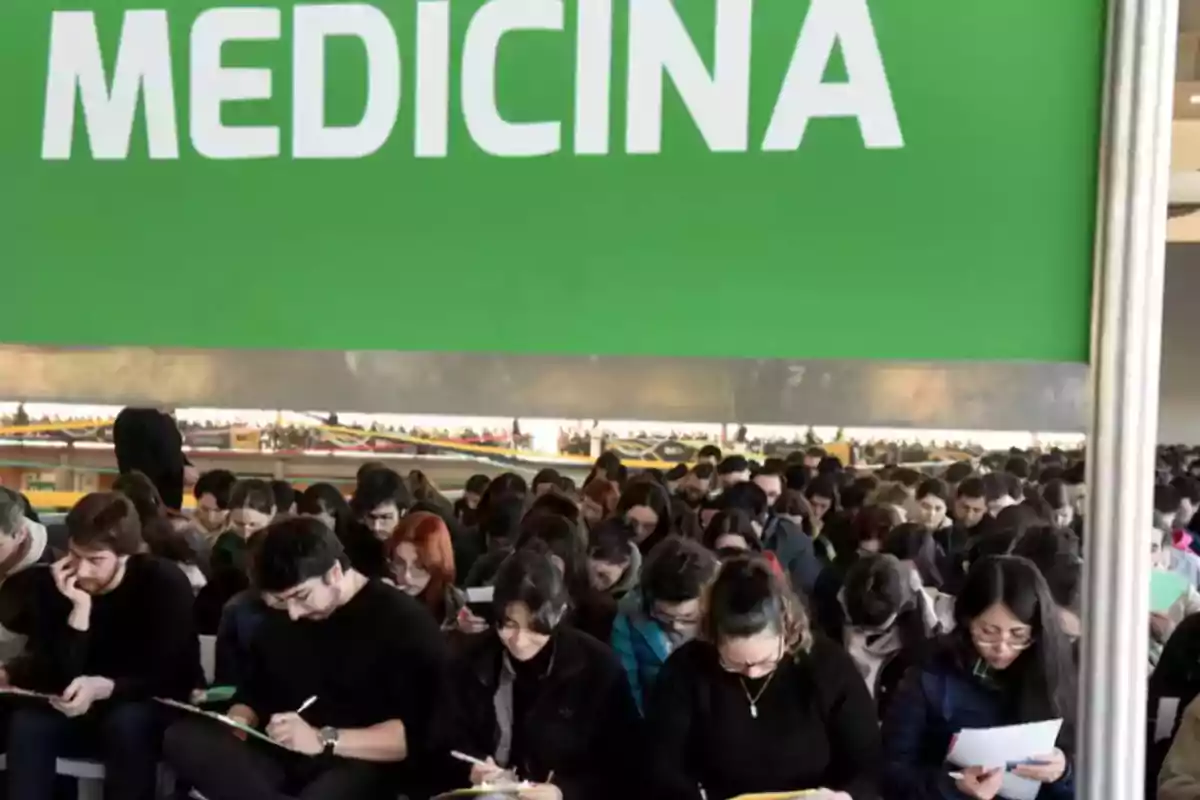 Estudiantes realizando un examen de admisión bajo un letrero verde que dice medicina Estudiantes realizando un examen de admisión bajo un letrero verde que dice medicina