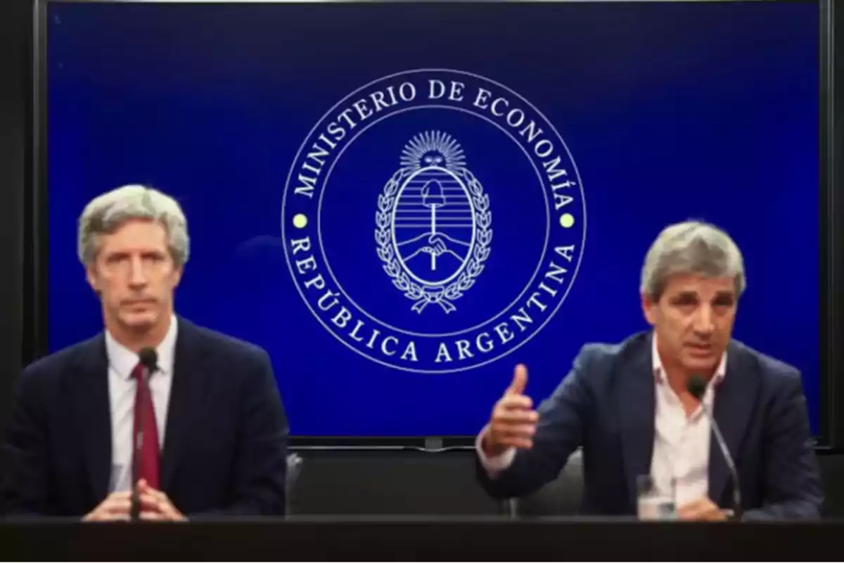 Dos hombres de traje en una conferencia de prensa frente a una pantalla azul con el logo del Ministerio de Economía de la República Argentina Dos hombres de traje en una conferencia de prensa frente a una pantalla azul con el logo del Ministerio de Economía de la República Argentina