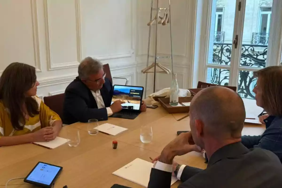 Cuatro personas sentadas alrededor de una mesa en una sala de reuniones mientras una de ellas muestra una presentación en una laptop