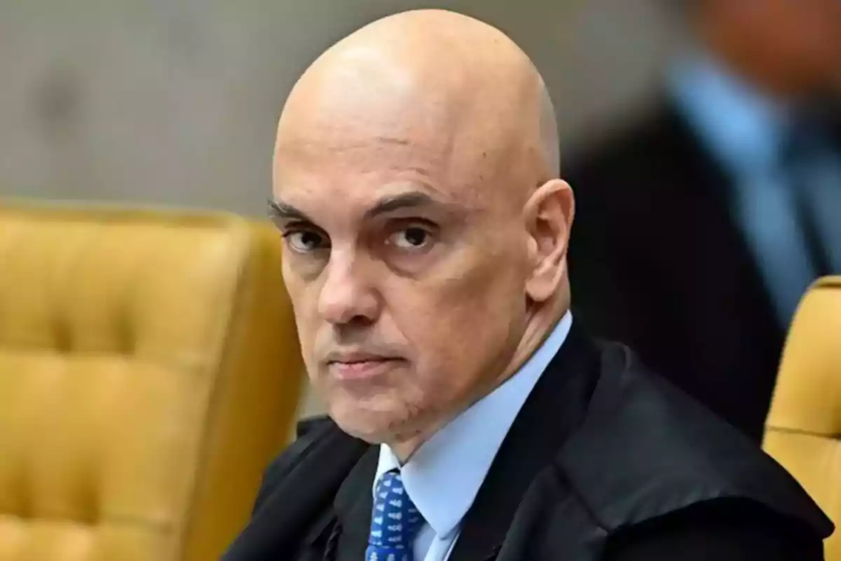 Hombre calvo con traje y corbata azul sentado en una silla amarilla mirando hacia la cámara Hombre calvo con traje y corbata azul sentado en una silla amarilla mirando hacia la cámara