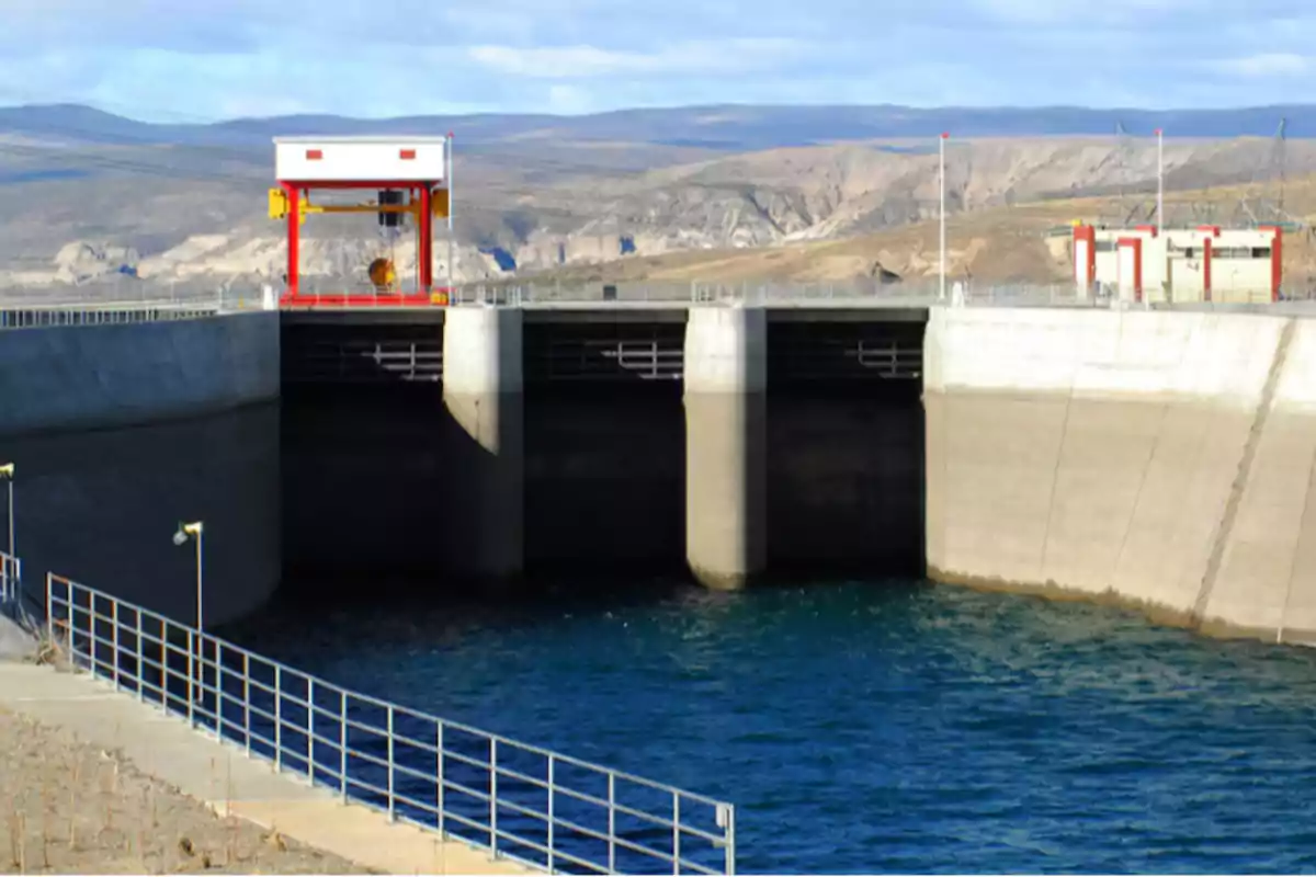 Vista frontal de una represa hidroeléctrica con agua azul en primer plano y montañas al fondo