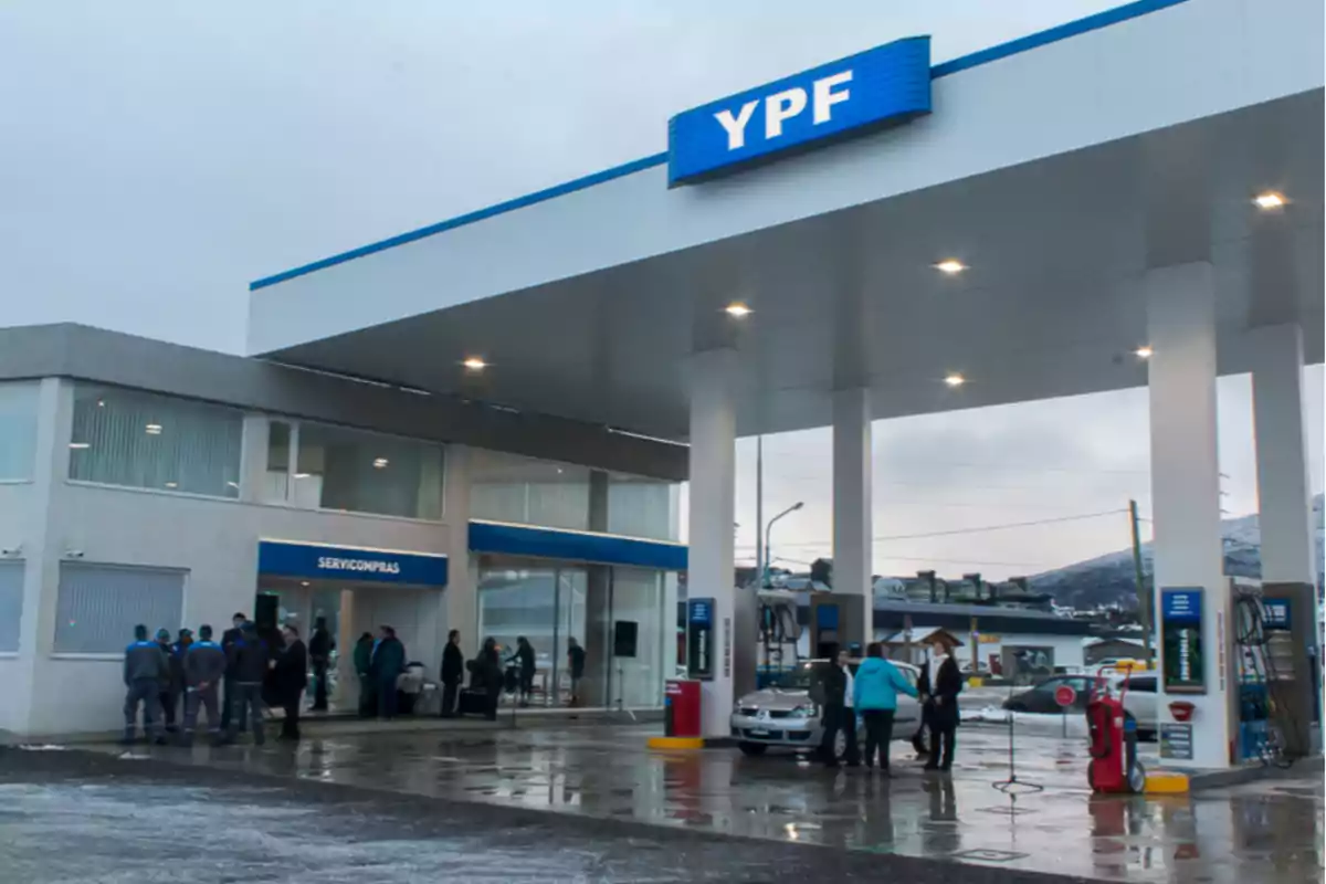 Estación de servicio YPF con varias personas y autos bajo el techo en un día nublado