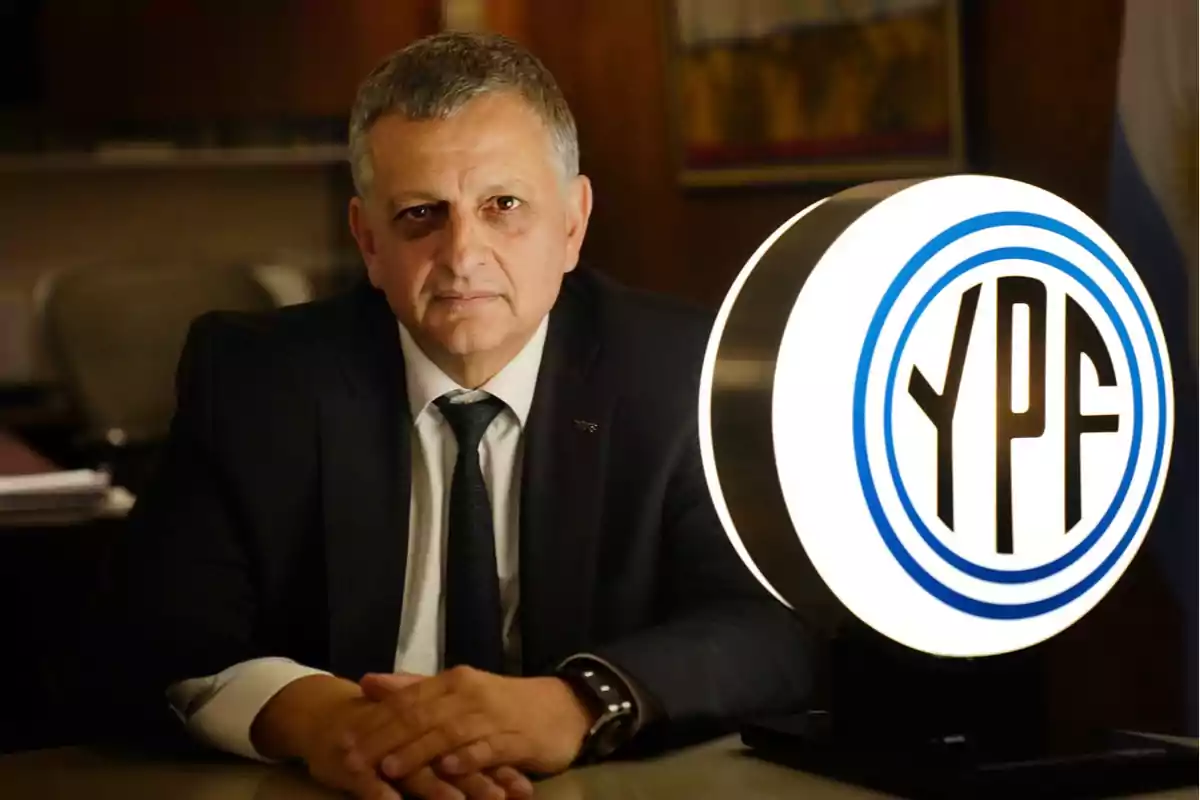 Hombre de traje sentado en una oficina junto a un logo iluminado de YPF Hombre de traje sentado en una oficina junto a un logo iluminado de YPF