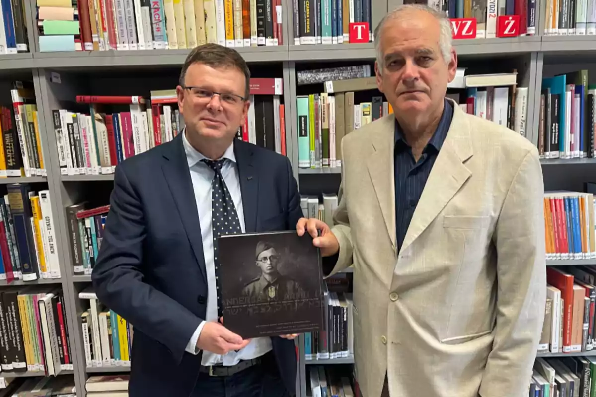 Dos hombres posan en una biblioteca mientras sostienen un libro con la imagen de un soldado en la portada Dos hombres posan en una biblioteca mientras sostienen un libro con la imagen de un soldado en la portada