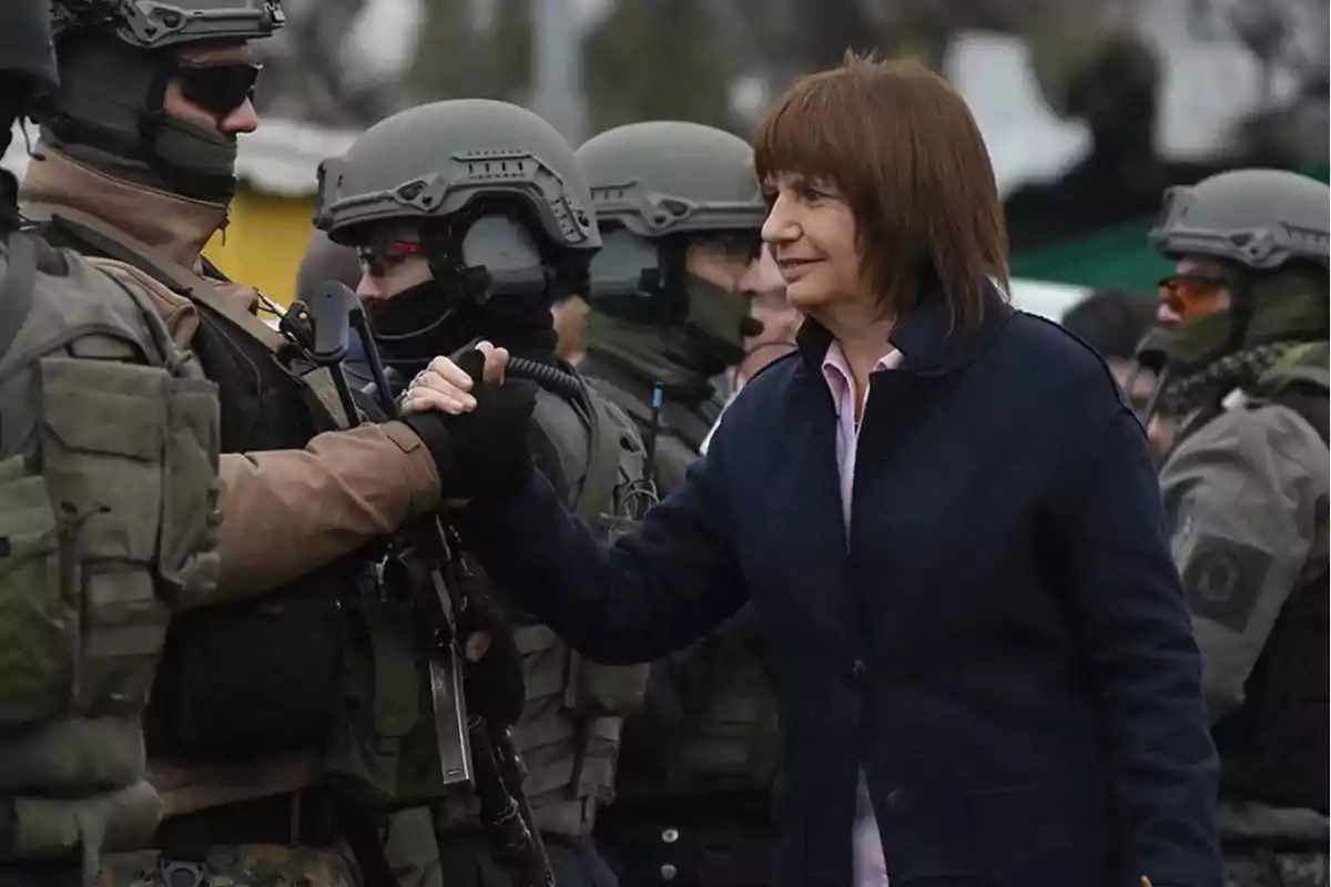 Una mujer vestida con abrigo oscuro saluda con un apretón de manos a un miembro de un grupo de fuerzas de seguridad que lleva uniforme táctico y casco mientras otros agentes están formados en el fondo Una mujer vestida con abrigo oscuro saluda con un apretón de manos a un miembro de un grupo de fuerzas de seguridad que lleva uniforme táctico y casco mientras otros agentes están formados en el fondo
