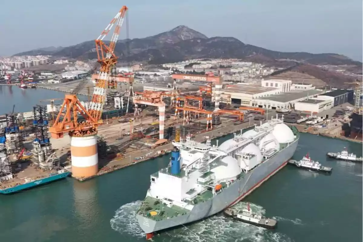 A large liquefied natural gas carrier is escorted by tugboats in an industrial shipyard with cranes and mountains in the background. A large liquefied natural gas carrier is escorted by tugboats in an industrial shipyard with cranes and mountains in the background.