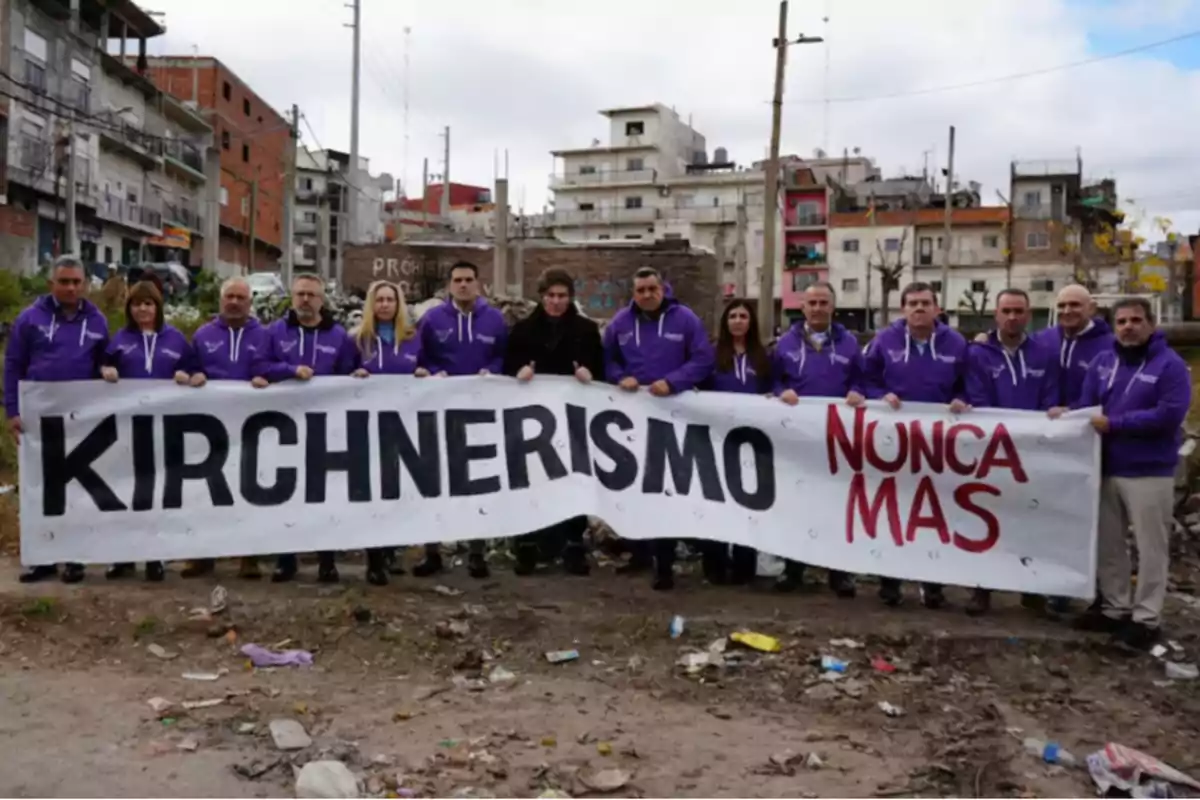 Group of people in purple sweatjerseys holding a banner that says "Kirchnerism never again" in an urban neighborhood