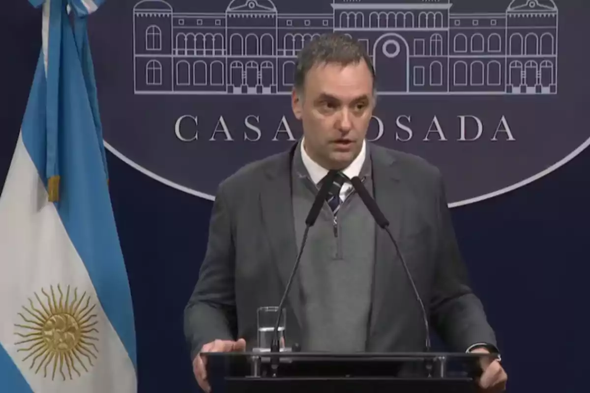 Un hombre de traje habla en una conferencia de prensa en la Casa Rosada junto a una bandera de Argentina Un hombre de traje habla en una conferencia de prensa en la Casa Rosada junto a una bandera de Argentina