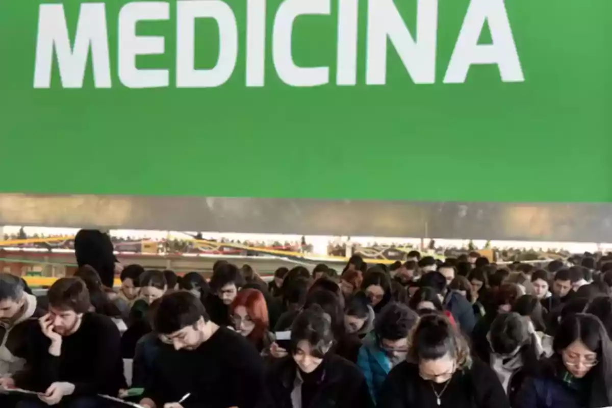 Un grupo numeroso de estudiantes concentrados escribiendo bajo un gran letrero verde que dice medicina