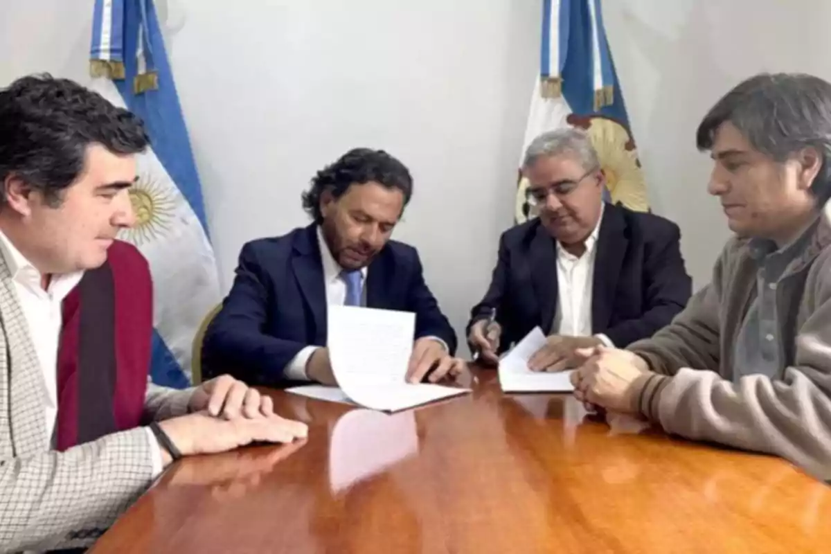 Four men sitting around a wooden table sign official documents with Argentine flags in the background. Four men sitting around a wooden table sign official documents with Argentine flags in the background.