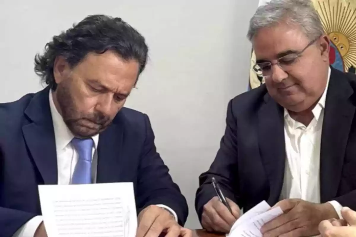 Two men in suits signing documents at a table