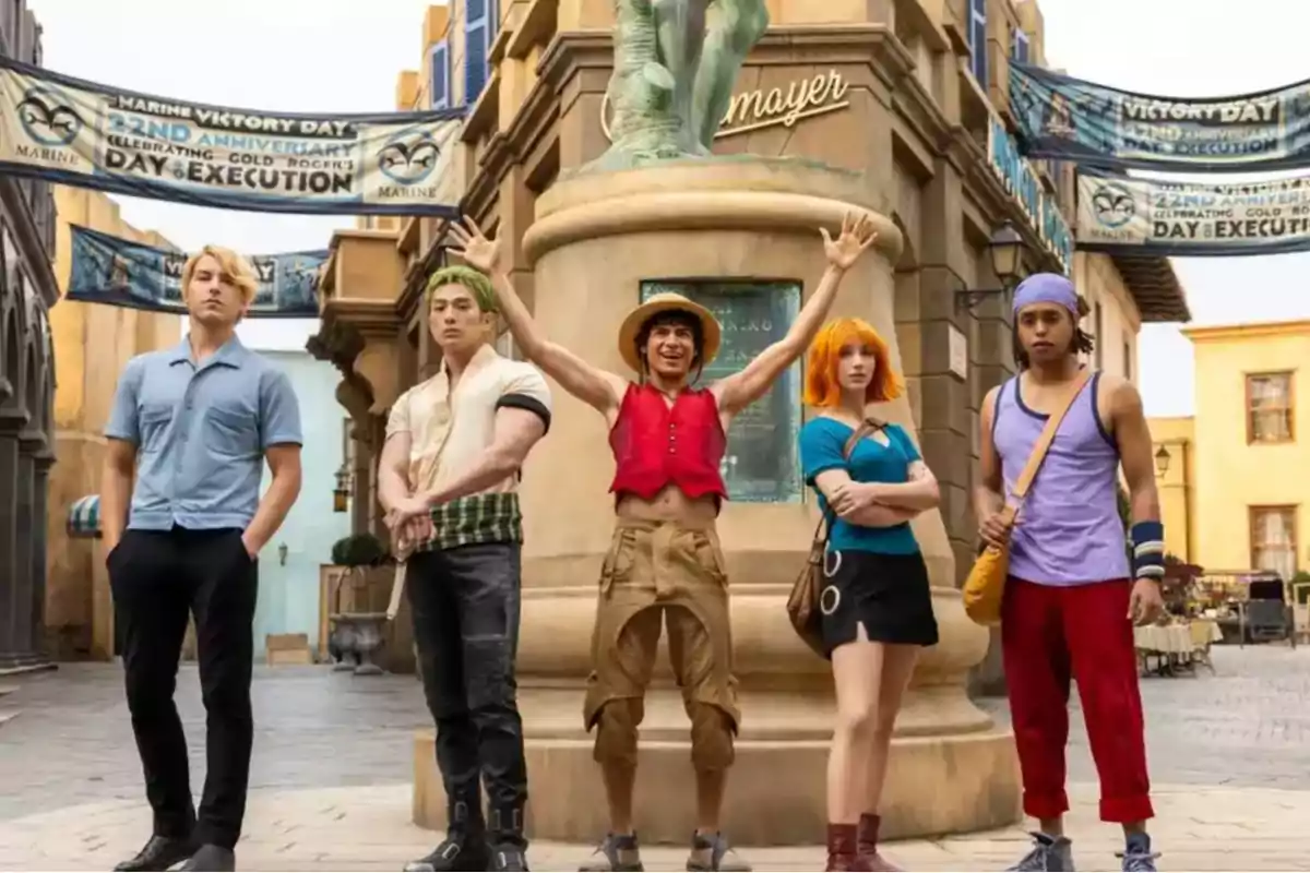 Five people dressed as anime characters pose in front of a statue in an urban plaza.