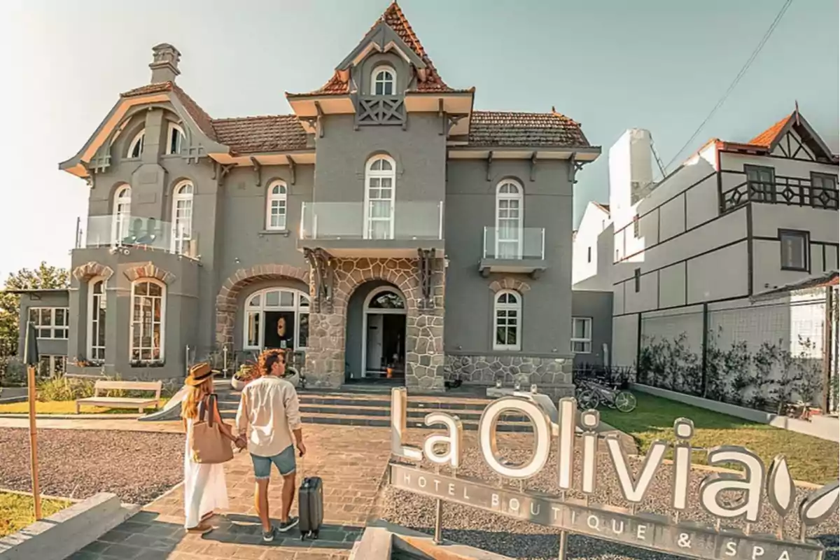 Pareja llegando con maleta a un hotel boutique de fachada gris y estilo clásico llamado La Olivia