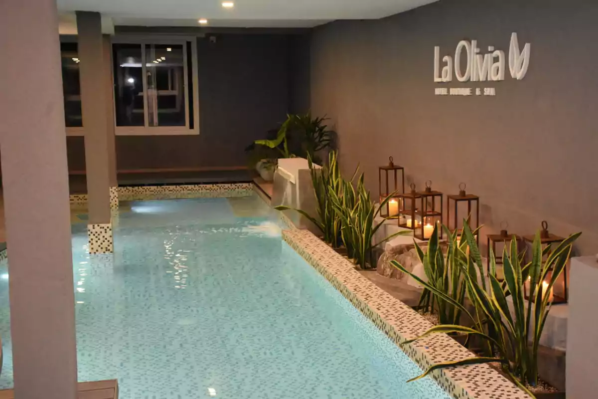 Piscina interior iluminada con plantas decorativas y faroles con velas junto a una pared con el letrero La Olivia Hotel Boutique & Spa Piscina interior iluminada con plantas decorativas y faroles con velas junto a una pared con el letrero La Olivia Hotel Boutique & Spa
