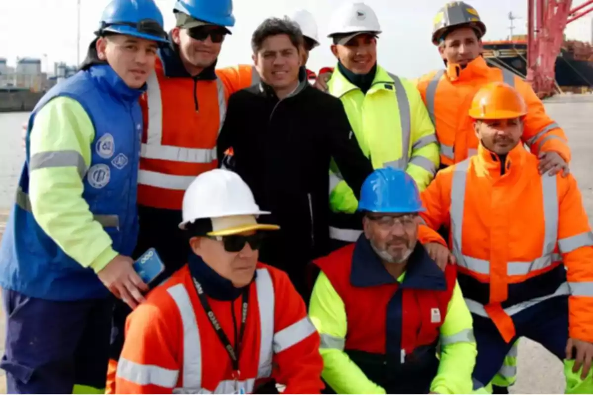 Grupo de trabajadores portuarios con cascos y chalecos de seguridad posando juntos al aire libre en una zona industrial
