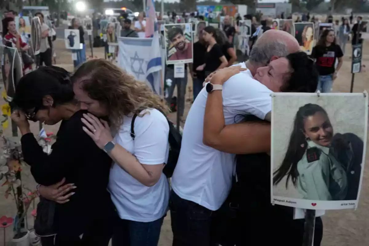 People hugging and comforting each other at an outdoor memorial with portraits of victims and an Israeli flag in the background People hugging and comforting each other at an outdoor memorial with portraits of victims and an Israeli flag in the background