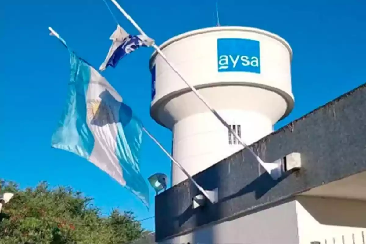 Tanque de agua de la empresa AySA junto a una bandera argentina ondeando bajo un cielo despejado Tanque de agua de la empresa AySA junto a una bandera argentina ondeando bajo un cielo despejado