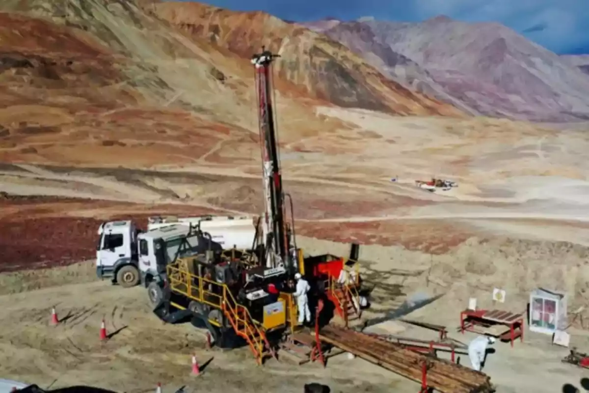Equipo de perforación minera operando en una zona montañosa árida con trabajadores y camiones alrededor Equipo de perforación minera operando en una zona montañosa árida con trabajadores y camiones alrededor