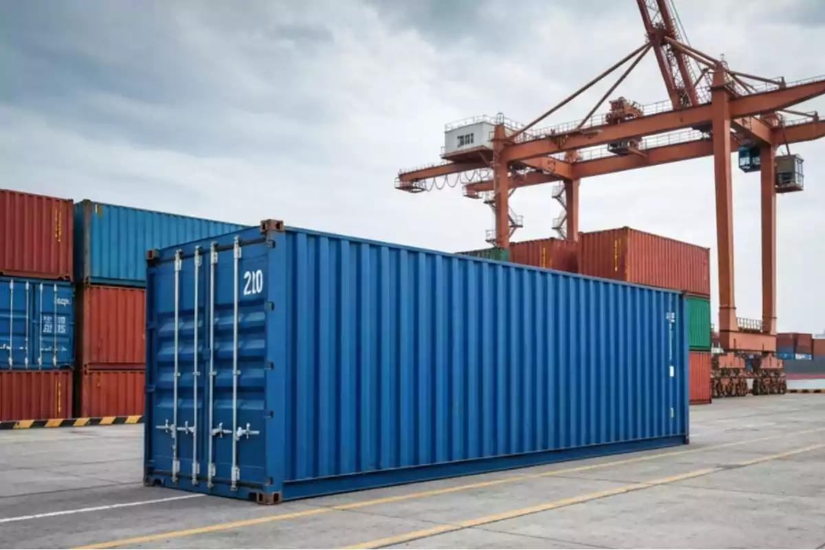 Blue container at a port surrounded by other containers and an industrial crane in the background