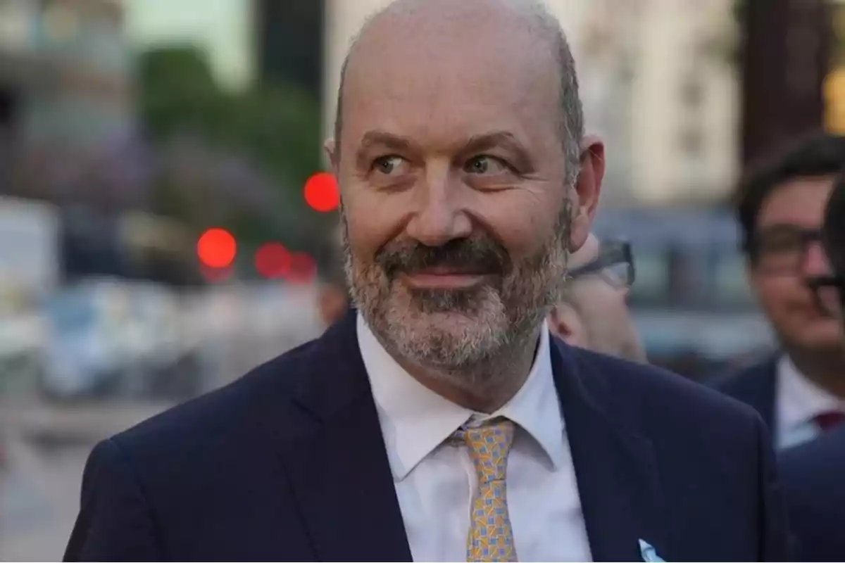 Hombre calvo con barba y traje sonríe mientras está al aire libre en una ciudad con luces desenfocadas al fondo Hombre calvo con barba y traje sonríe mientras está al aire libre en una ciudad con luces desenfocadas al fondo