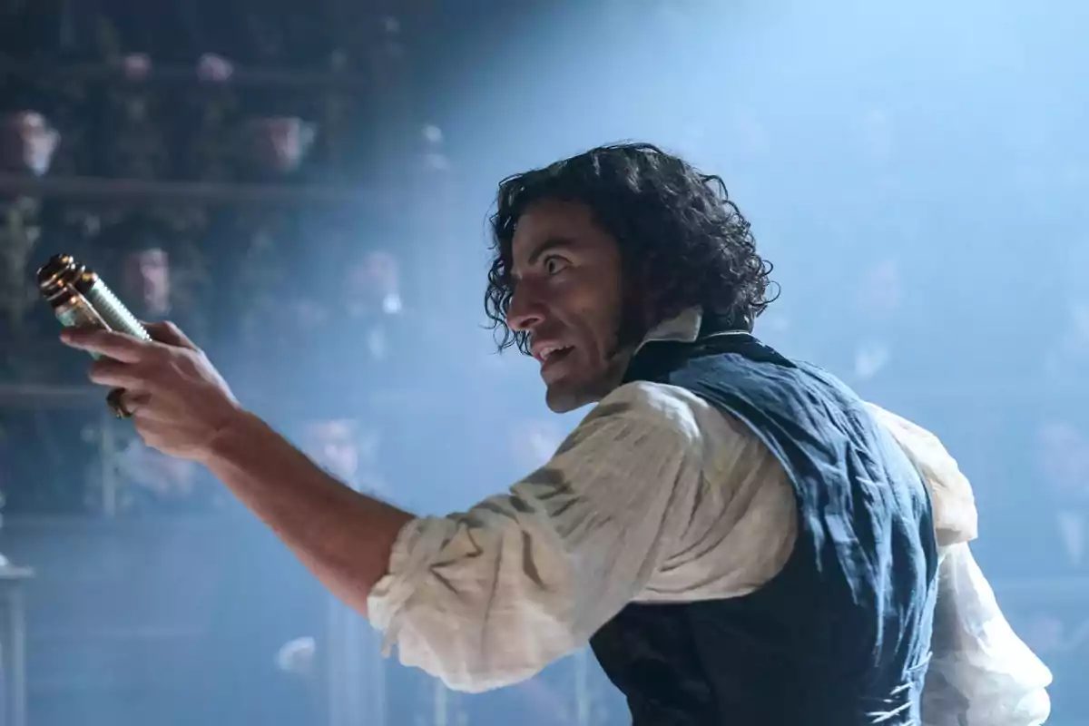 Curly-haired man in old-fashioned clothing holds a cylindrical object while speaking passionately in a room full of spectators. Curly-haired man in old-fashioned clothing holds a cylindrical object while speaking passionately in a room full of spectators.