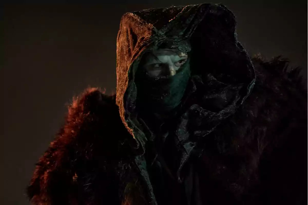 Person wearing a dark hood and a scarf covering their face in a gloomy environment