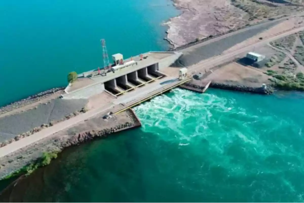 Aerial view of a dam with open gates and water flowing into a river surrounded by arid land