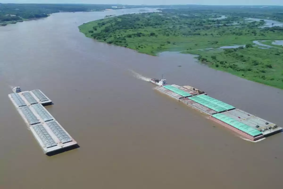 Aerial view of two barges sailing on a wide river surrounded by vegetation and green fields