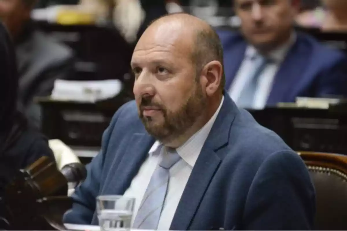 Bald man with a beard and a blue jacket sitting in what appears to be a meeting room or parliament. Bald man with a beard and a blue jacket sitting in what appears to be a meeting room or parliament.