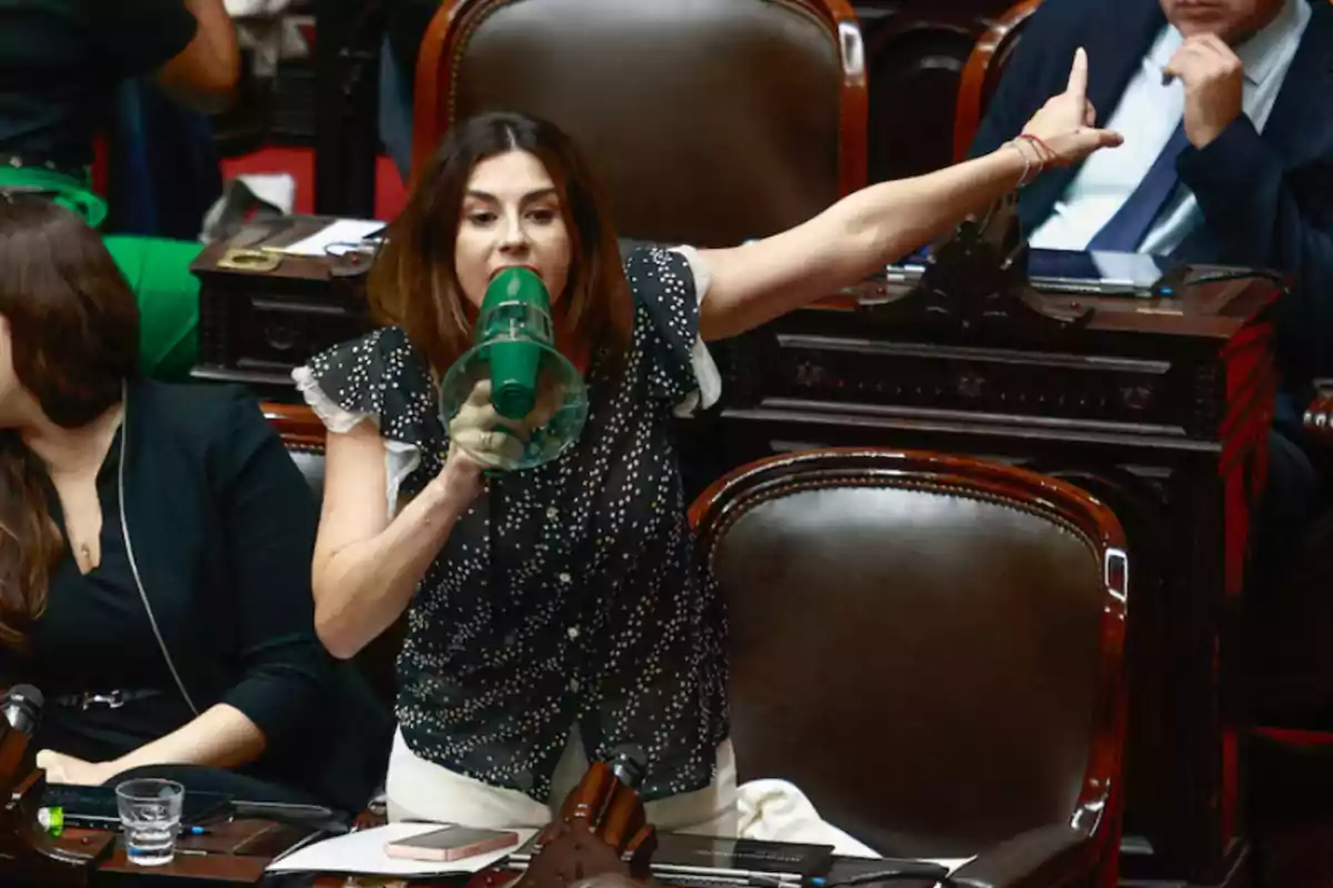 Woman speaking through a megaphone and pointing with her arm extended in a parliamentary chamber Woman speaking through a megaphone and pointing with her arm extended in a parliamentary chamber
