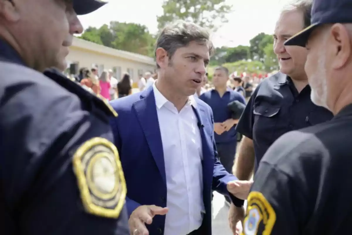 Un hombre de traje azul conversa con varios policías en un evento al aire libre con personas al fondo Un hombre de traje azul conversa con varios policías en un evento al aire libre con personas al fondo