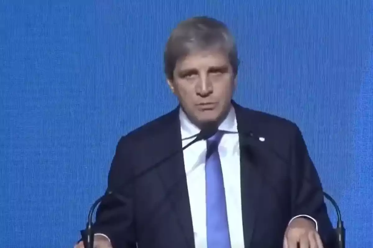 Gray-haired man in a dark suit and blue tie speaking in front of a microphone with a blue background Gray-haired man in a dark suit and blue tie speaking in front of a microphone with a blue background