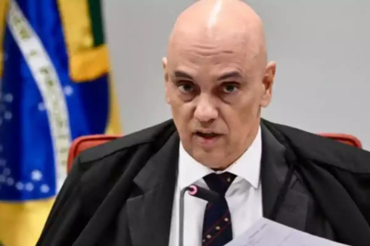 Bald man in a black robe speaking in front of a microphone with a Brazilian flag in the background Bald man in a black robe speaking in front of a microphone with a Brazilian flag in the background