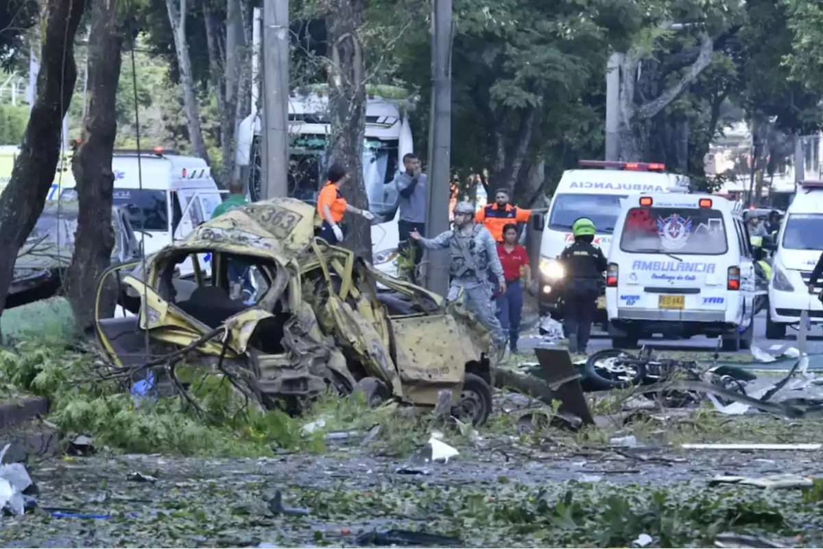 Un taxi completamente destruido en medio de una calle con ramas y escombros mientras varias ambulancias y personal de emergencia atienden la situación Un taxi completamente destruido en medio de una calle con ramas y escombros mientras varias ambulancias y personal de emergencia atienden la situación