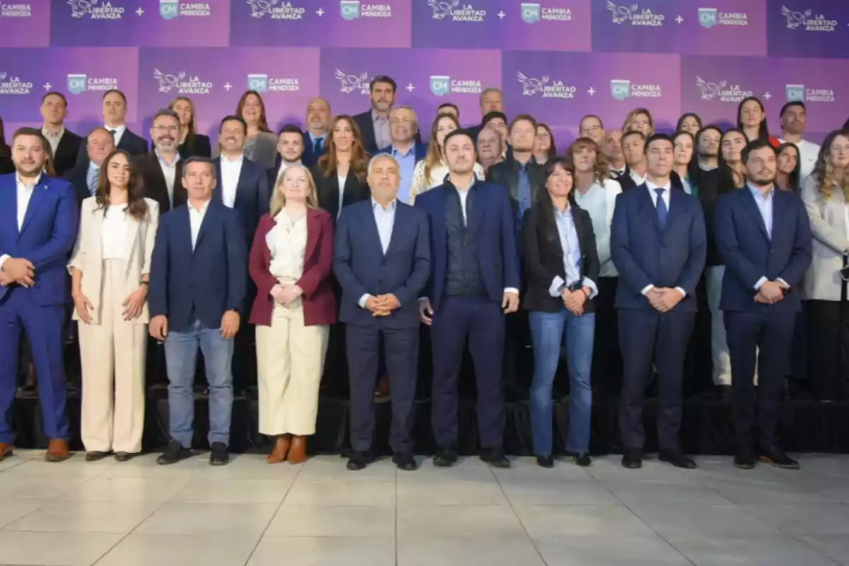 Un grupo numeroso de personas posando para una foto formal frente a un fondo violeta con logotipos de Cambia Mendoza y La Libertad Avanza