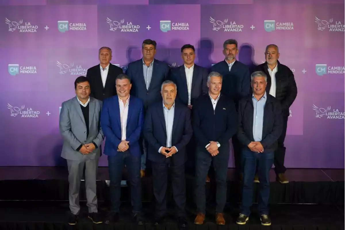 Nueve hombres posan en grupo sobre un escenario con fondo violeta que tiene los logos de La Libertad Avanza y Cambia Mendoza Nueve hombres posan en grupo sobre un escenario con fondo violeta que tiene los logos de La Libertad Avanza y Cambia Mendoza
