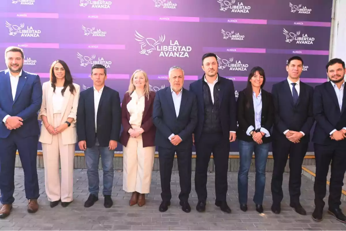 Grupo de personas posando frente a un fondo violeta con el logo y texto de La Libertad Avanza Grupo de personas posando frente a un fondo violeta con el logo y texto de La Libertad Avanza