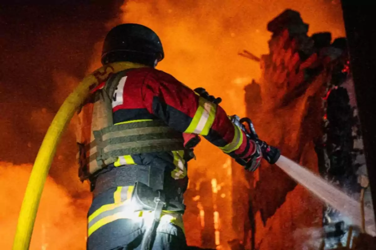 Firefighter battling a blaze with a water hose while the fire engulfs a building in the background. Firefighter battling a blaze with a water hose while the fire engulfs a building in the background.