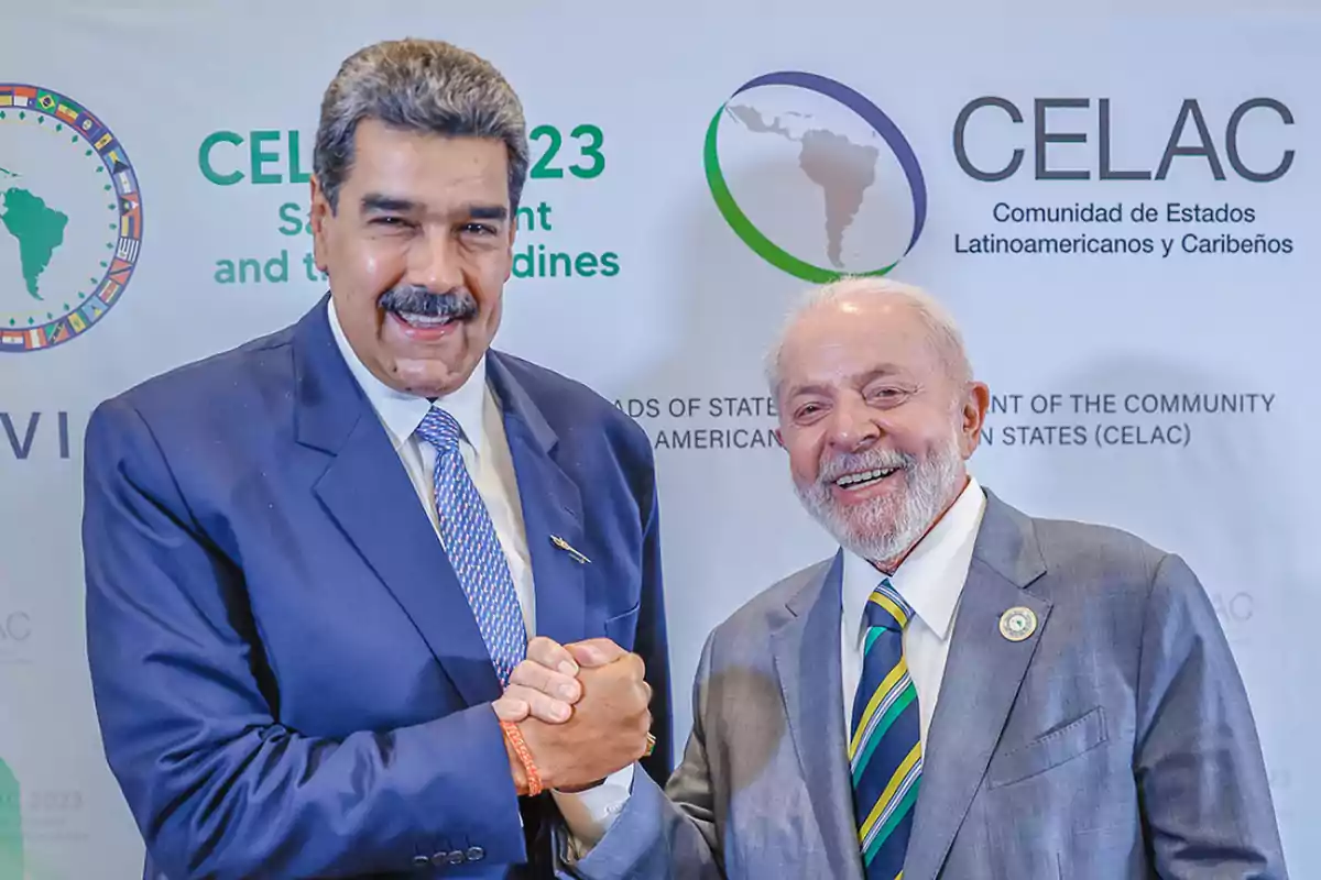 Two men in suits smile and shake hands in front of a backdrop with CELAC logos. Two men in suits smile and shake hands in front of a backdrop with CELAC logos.