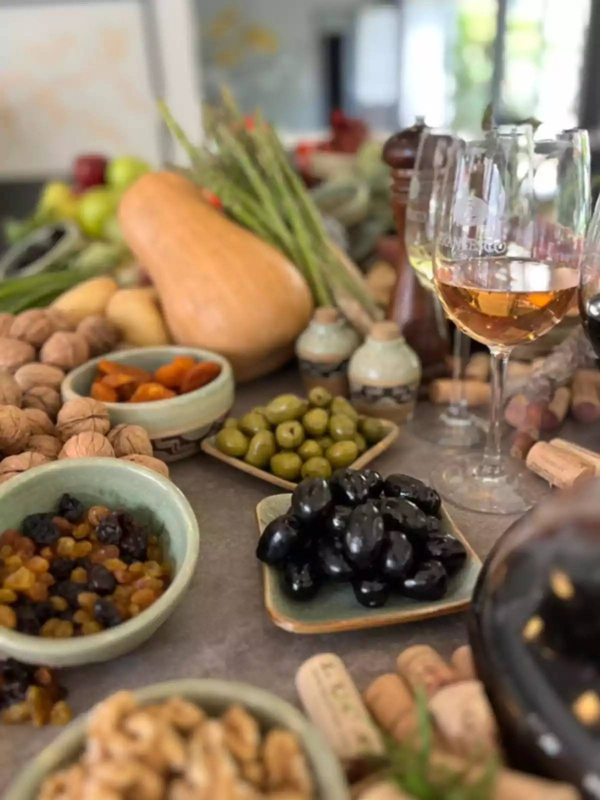 Mesa con copas de vino, aceitunas, frutos secos, nueces, pasas, espárragos y una calabaza, todo dispuesto para una degustación gourmet Mesa con copas de vino, aceitunas, frutos secos, nueces, pasas, espárragos y una calabaza, todo dispuesto para una degustación gourmet