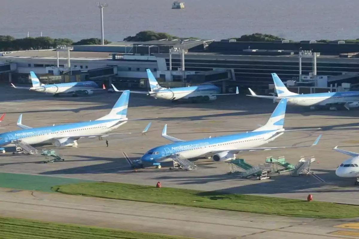 Varios aviones de Aerolíneas Argentinas estacionados en la pista de un aeropuerto junto a la terminal
