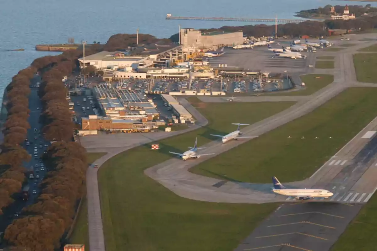Vista aérea de un aeropuerto junto al río con varios aviones en pista y estacionados, rodeado de áreas verdes y una carretera arbolada. Vista aérea de un aeropuerto junto al río con varios aviones en pista y estacionados, rodeado de áreas verdes y una carretera arbolada.