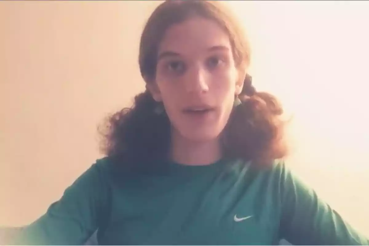 Persona con cabello largo y rizado recogido en dos coletas, usando una camiseta verde con el logo de Nike, mirando al frente en un ambiente iluminado. Persona con cabello largo y rizado recogido en dos coletas, usando una camiseta verde con el logo de Nike, mirando al frente en un ambiente iluminado.