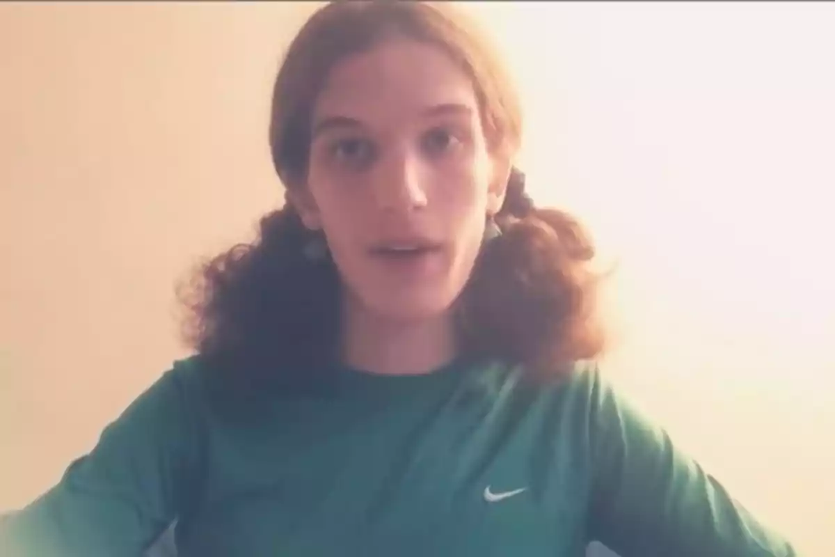 Young person with long, curly hair tied in two pigtails, wearing a green T-jersey with the Nike logo, in front of a light background. Young person with long, curly hair tied in two pigtails, wearing a green T-jersey with the Nike logo, in front of a light background.
